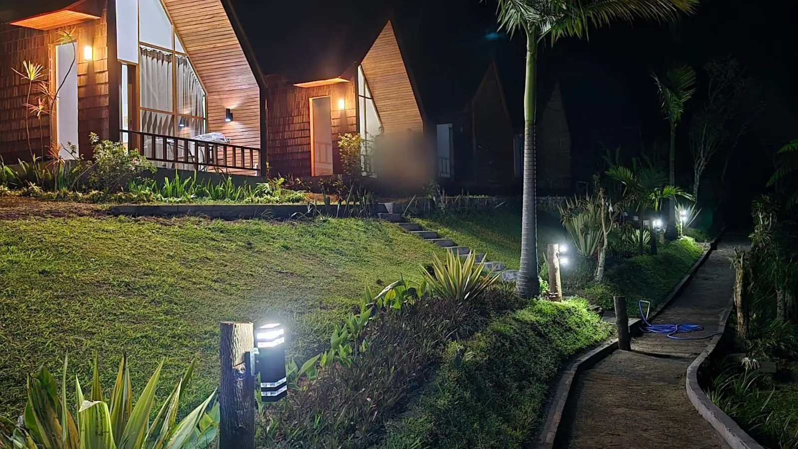 A-frame cabins at Catu Glamping lit up at night along the garden path