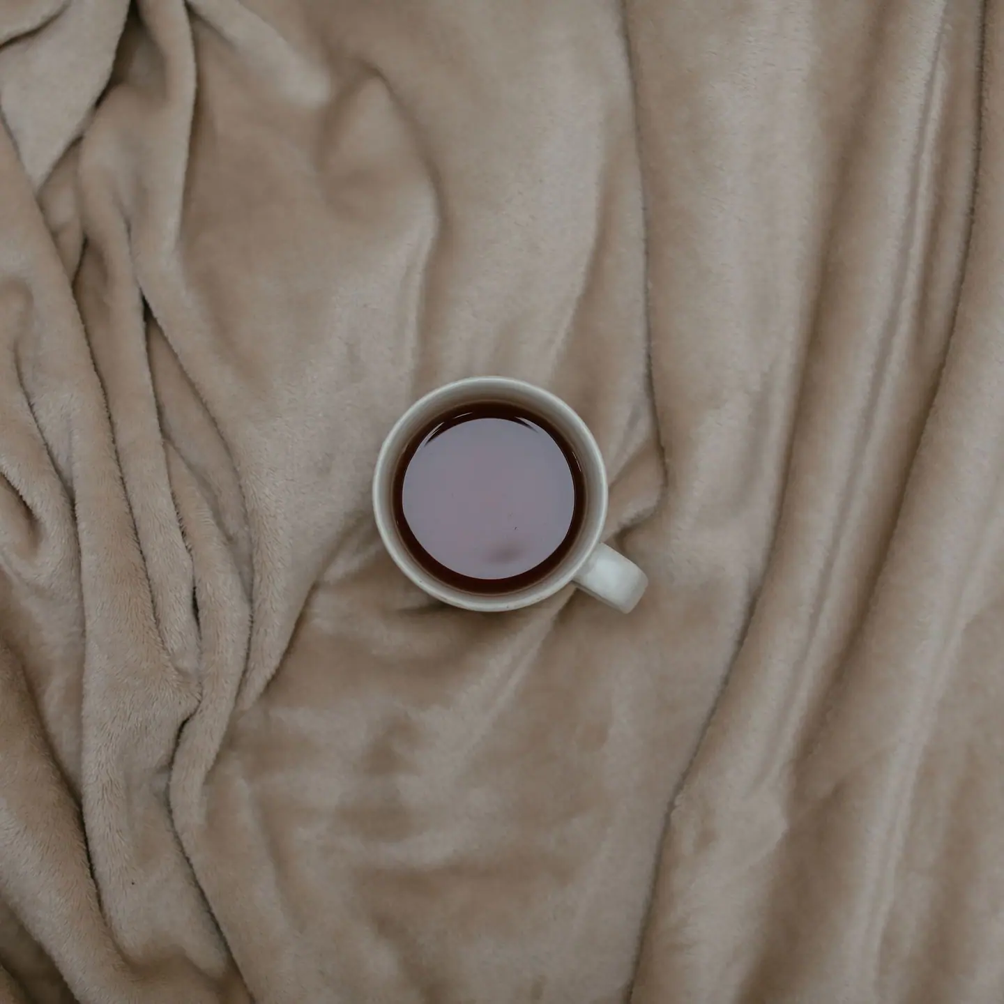 A cup of coffee on a soft beige blanket