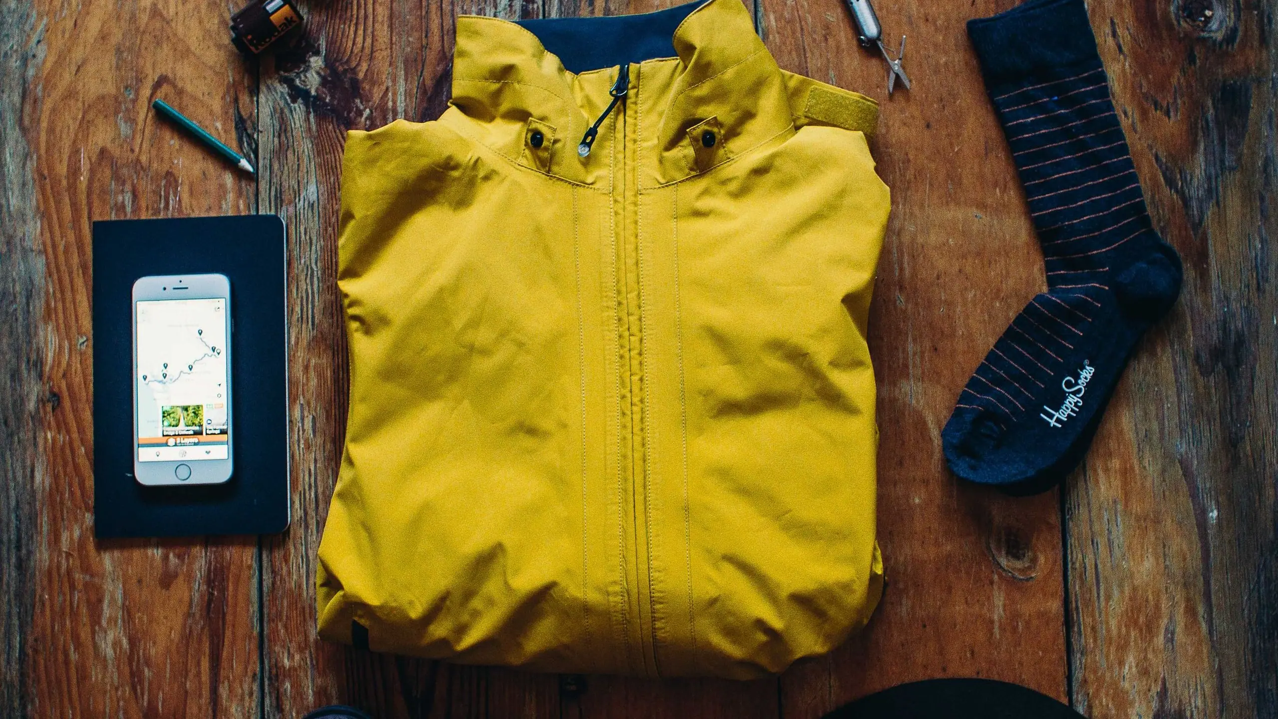 A rain jacket, socks, phone and notebook laid out on a wooden table